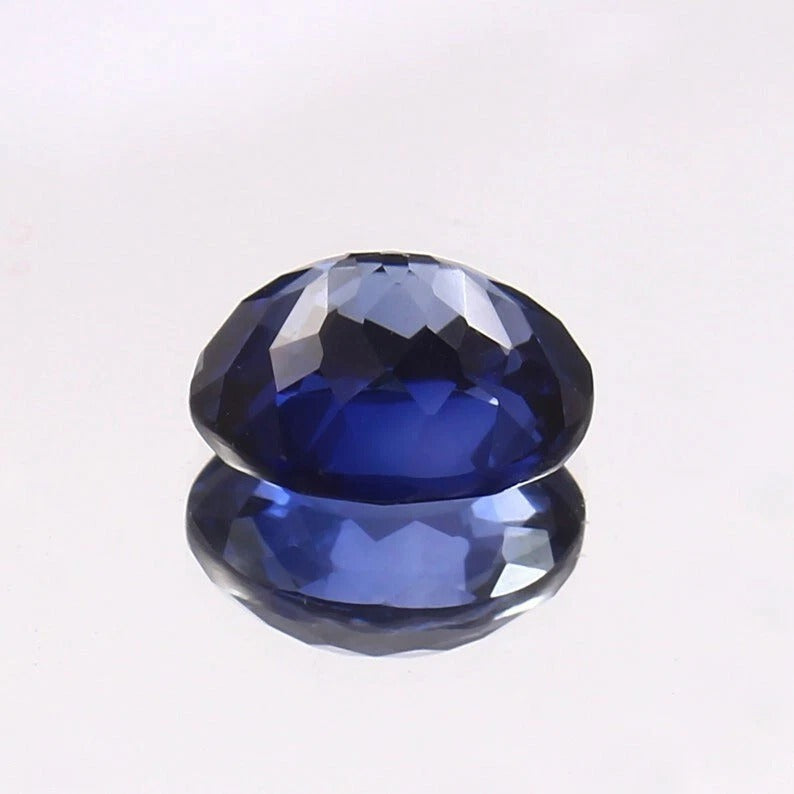 Faceted Royal Blue Sapphire gemstone on a reflective surface with a light gray background