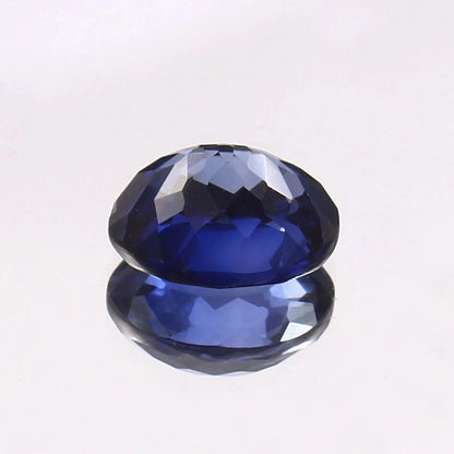 Faceted Royal Blue Sapphire gemstone on a reflective surface with a light gray background