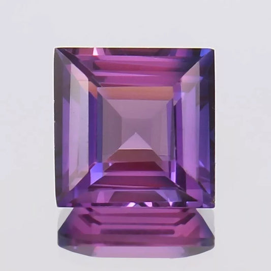 Faceted Purple Pink Ceylon Sapphire gemstone on a light gray background