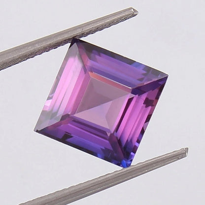 Faceted Purple Pink Ceylon Sapphire gemstone held between tweezers on a light gray background