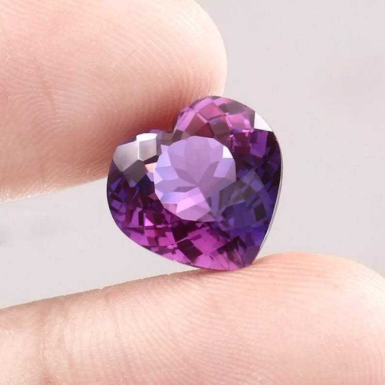 Heart-shaped Purple-Pink Sapphire gemstone held between fingers against a neutral background