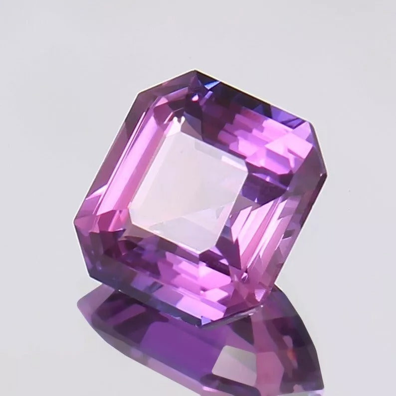 Faceted Purple Pink Sapphire gemstone on a light gray background