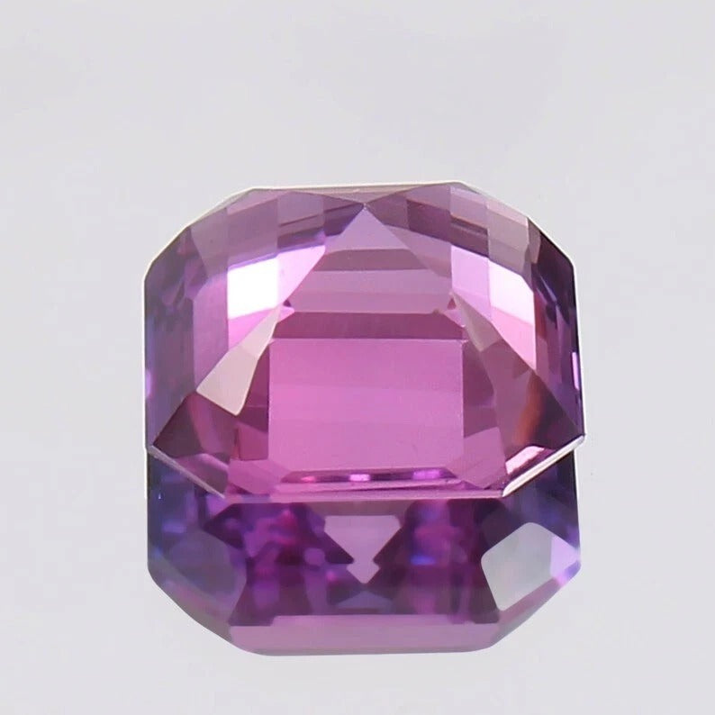 Faceted Purple Pink Sapphire gemstone on a light gray background