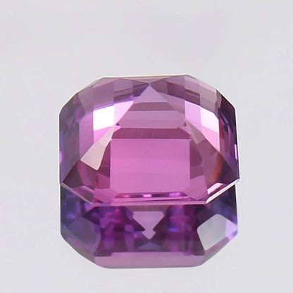 Faceted Purple Pink Sapphire gemstone on a light gray background