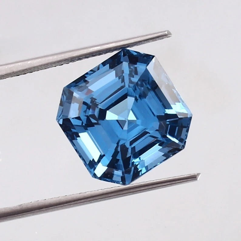 Swiss Blue Topaz gemstone held between tweezers on a light gray background