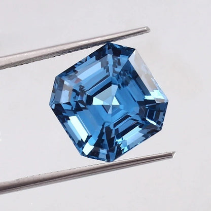 Swiss Blue Topaz gemstone held between tweezers on a light gray background