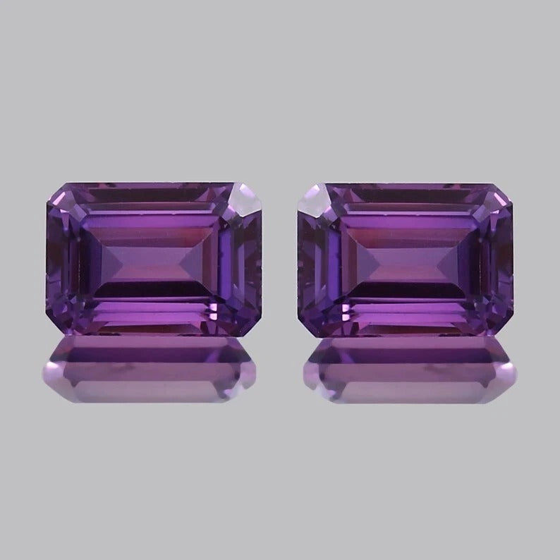 Pair Ceylon Purple Sapphire emerald-cut purple gemstones on a light gray background