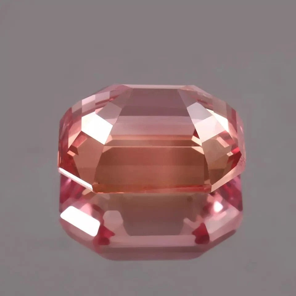 Faceted Peach-Pink Padparadscha Sapphire gemstone on a gray background