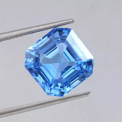 Ceylon Blue Spinel gemstone held by tweezers on a light gray background