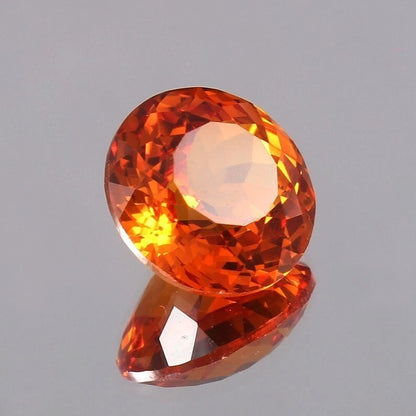 Faceted Orange Sapphire gemstone on a reflective gray surface