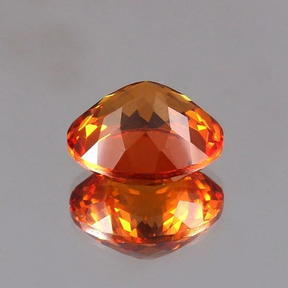 Faceted Orange Sapphire gemstone on a reflective gray surface