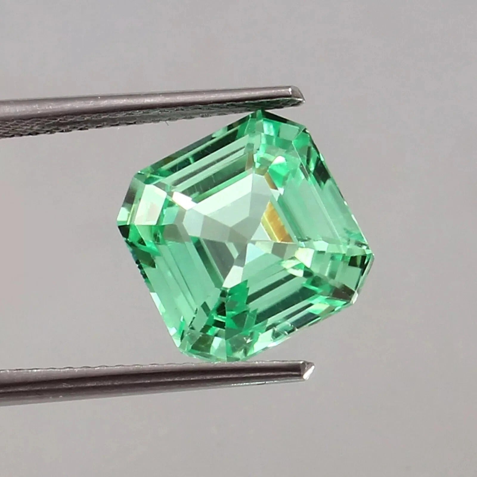 sapphire asscher cut green gemstone held by tweezers on a gray background