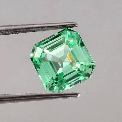sapphire asscher cut green gemstone held by tweezers on a gray background