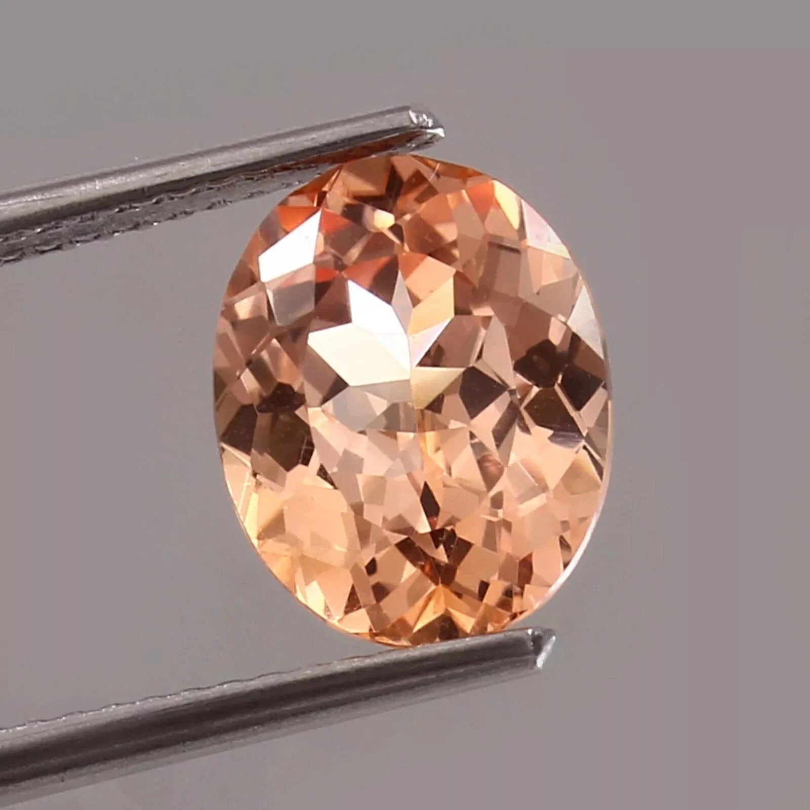 Round Peach Padparadscha Sapphire gemstone held between tweezers against a gray background