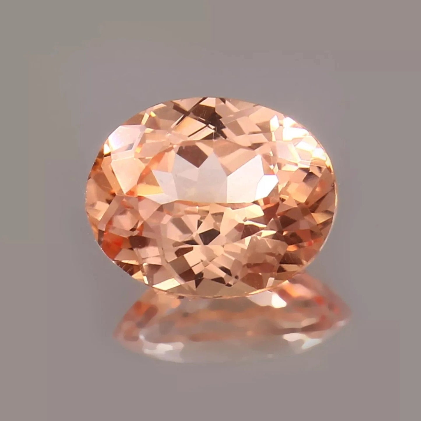 Peach Padparadscha Sapphire gemstone on a reflective gray surface