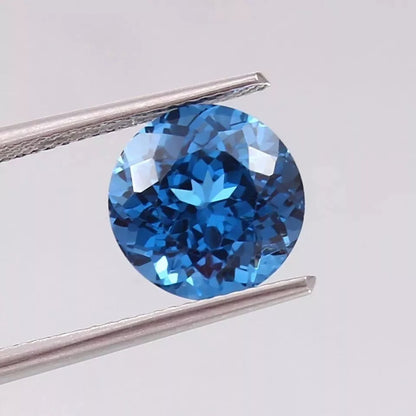 Indicolite Blue Color Tourmaline gemstone held by tweezers on a light gray background