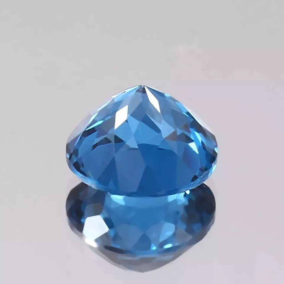 Faceted Indicolite Blue Color Tourmaline  gemstone on a reflective surface with a light gray background