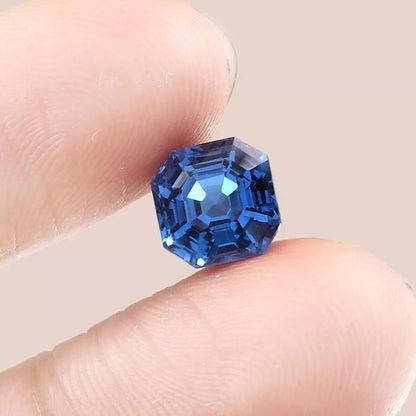 Blue  Indicolite Tourmaline gemstone held between two fingers against a neutral background