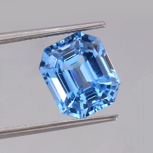 Blue sapphire gemstone held between tweezers on a gray background