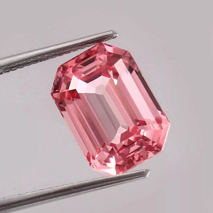 Padparadscha Sapphire Peach to Pink gemstone held between tweezers on a light gray background