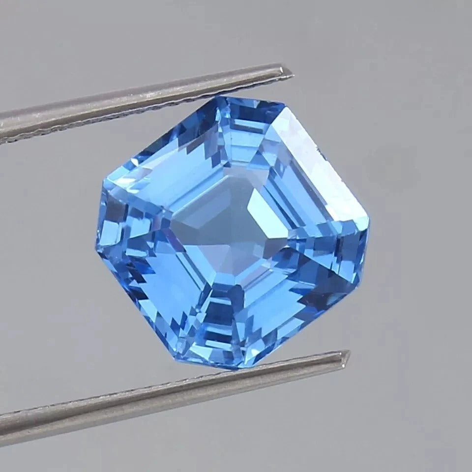Ceylon Blue Sapphire gemstone held between tweezers on a gray background