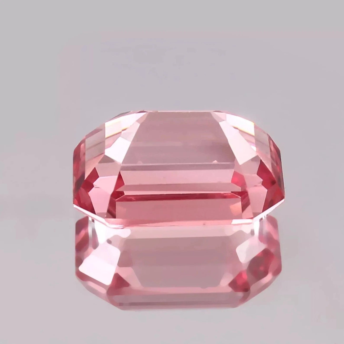 Faceted Padparadscha Sapphire Peach to Pink gemstone on a gray background