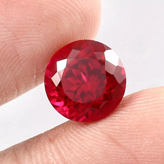 Round red Mozambique Ruby gemstone held between two fingers against a white background