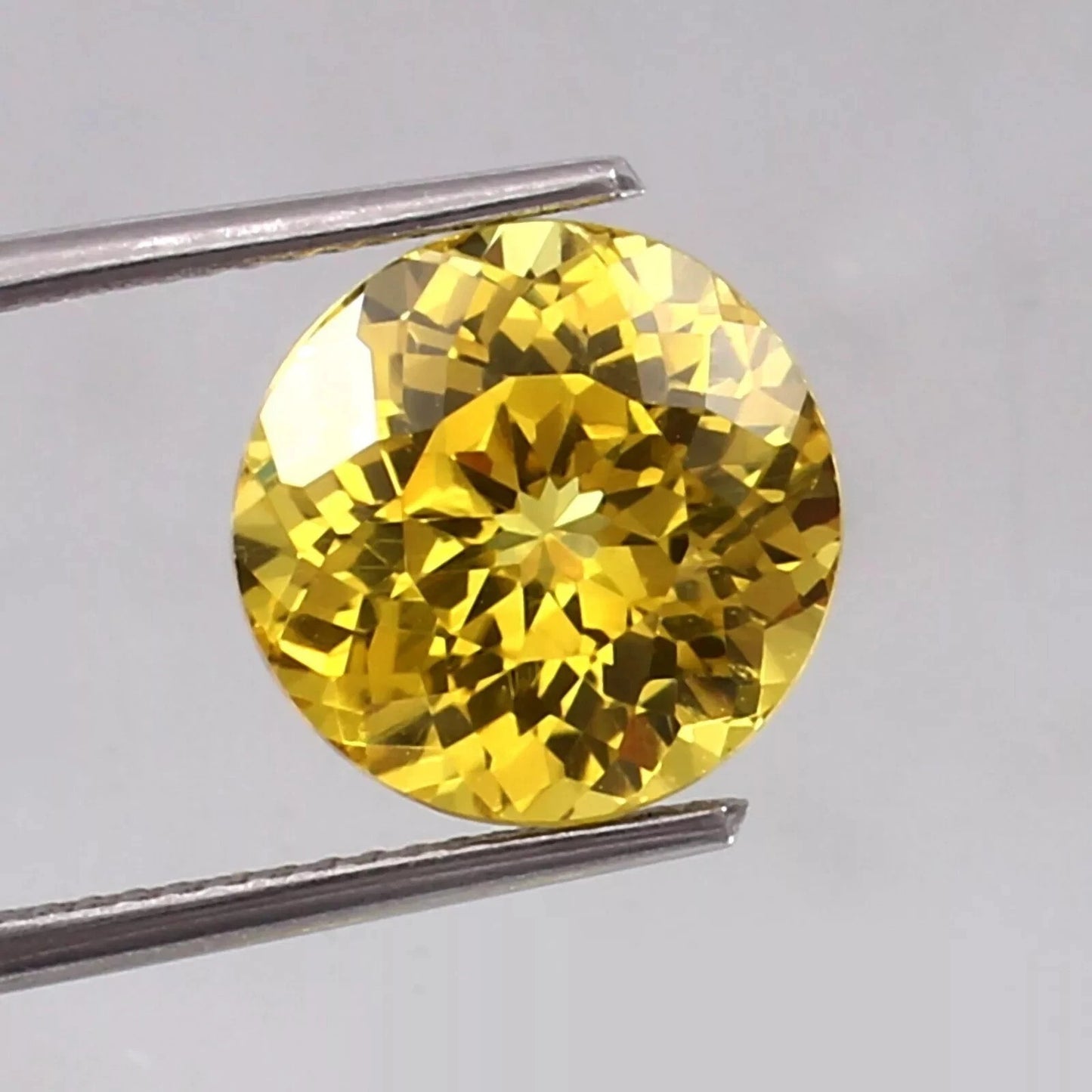 Ceylon Yellow Sapphire gemstone held between tweezers on a light gray background
