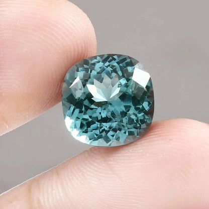 Teal Spinel  gemstone held between fingers against a neutral background