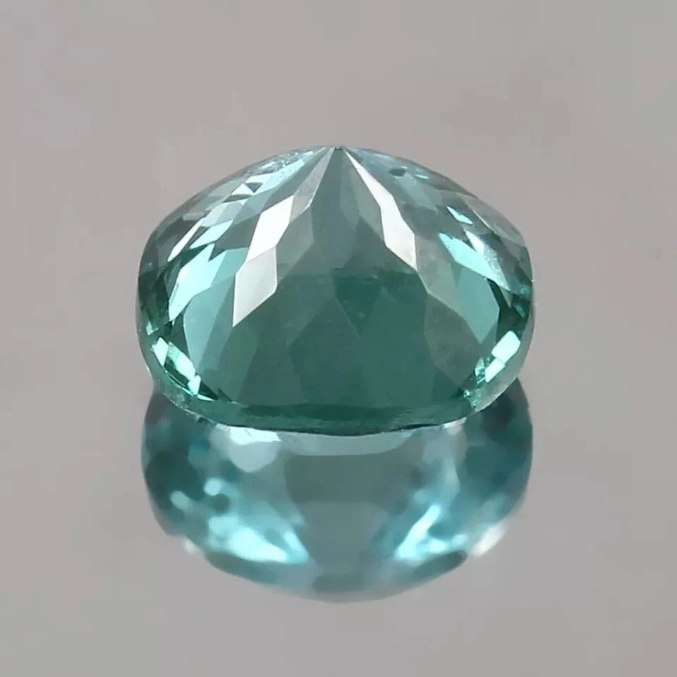 Faceted teal Spinel  gemstone on a reflective gray surface