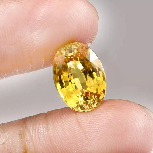 Yellow Sapphire gemstone held between fingers against a neutral background
