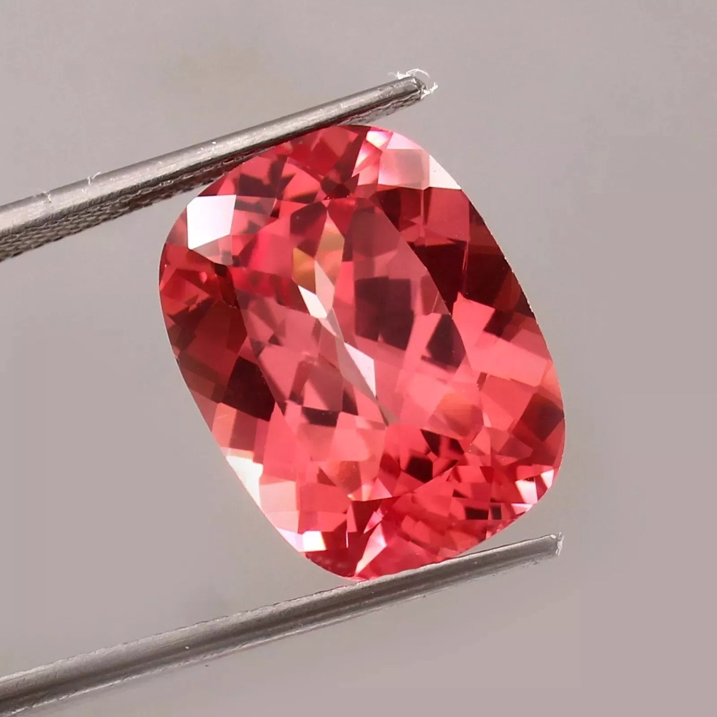 Padparadscha Sapphire gemstone held by tweezers on a gray background
