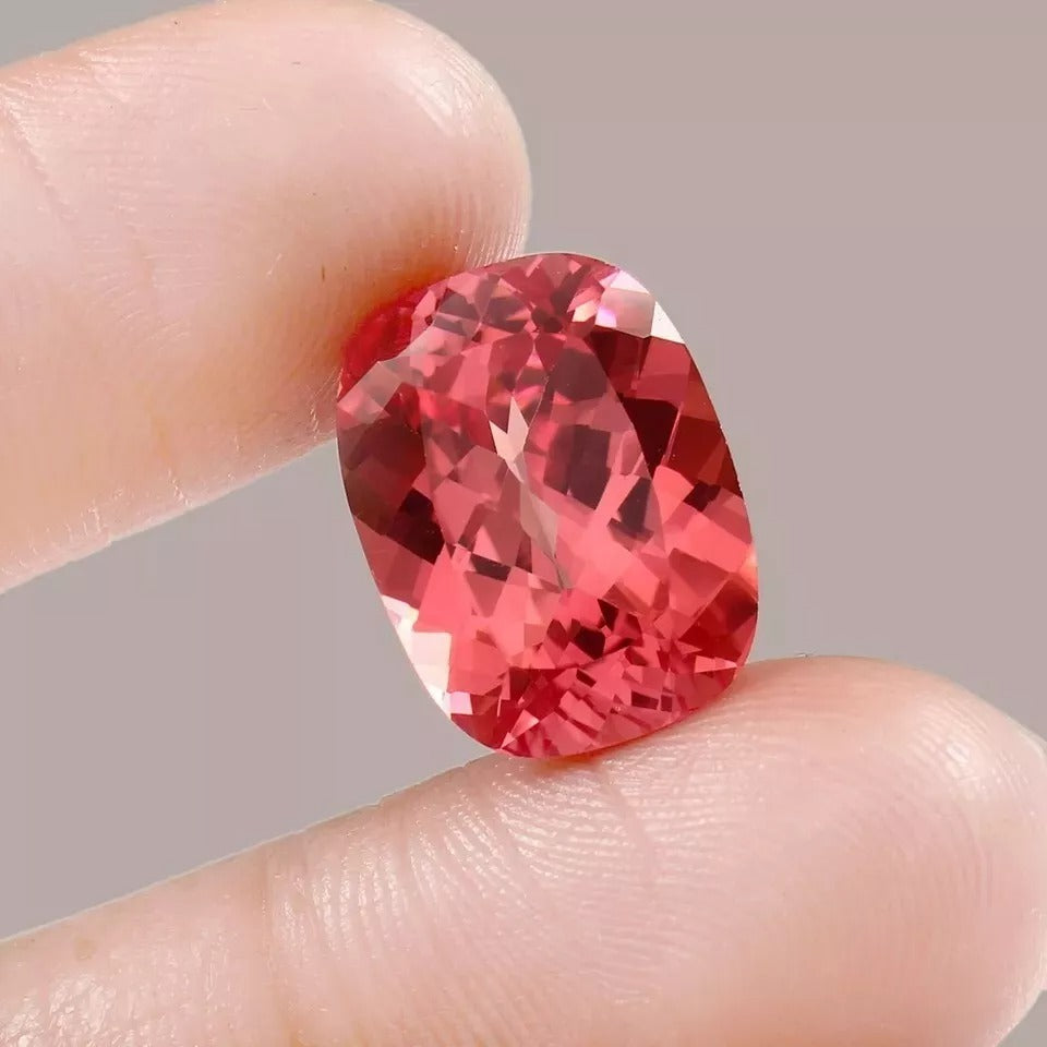 Padparadscha Sapphire gemstone held between fingers against a neutral background