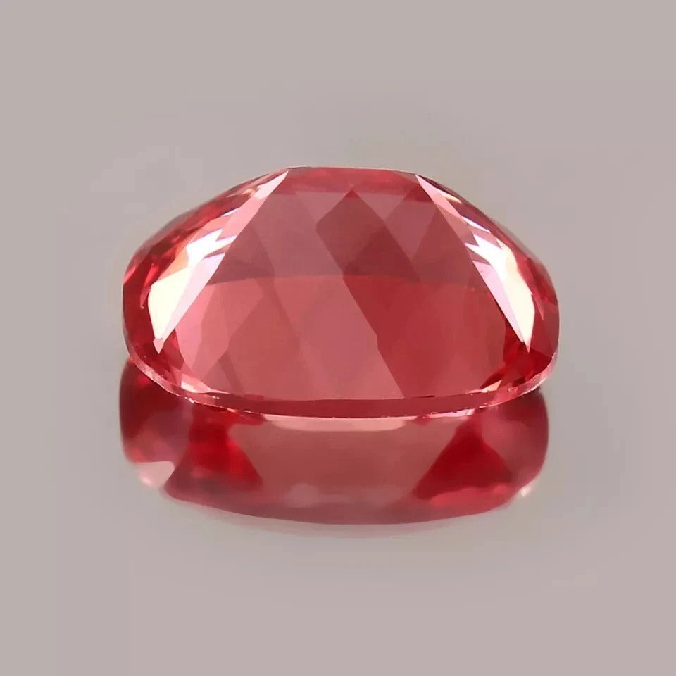 Faceted Padparadscha Sapphire gemstone on a gray background