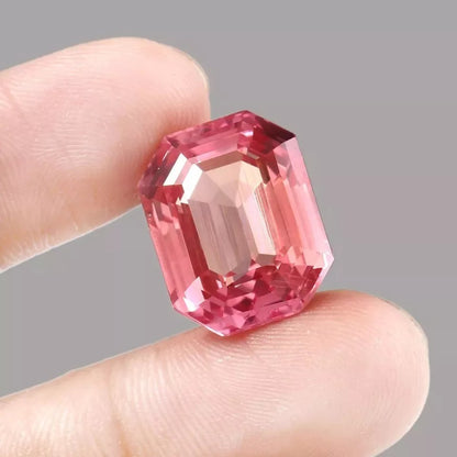 Peach-Pink Padparadscha Sapphire gemstone held between fingers against a gray background
