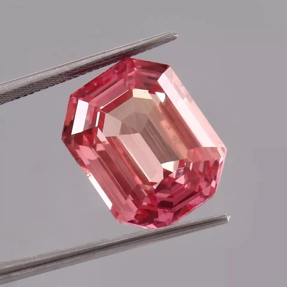 Peach-Pink Padparadscha Sapphire gemstone held by tweezers on a gray background