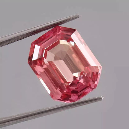 Peach-Pink Padparadscha Sapphire gemstone held by tweezers on a gray background