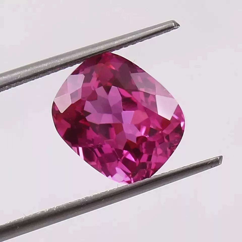 Faceted Pink sapphire gemstone held between tweezers against a light gray background